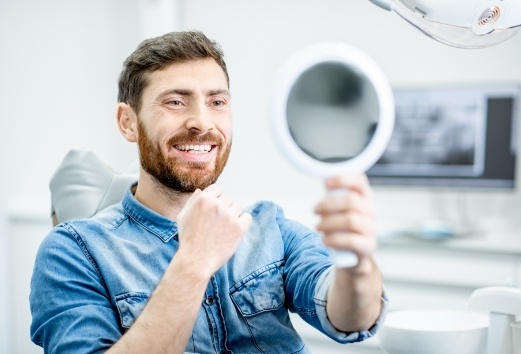 Man looking at healthy smile in  mirror after preventive dentistry visit