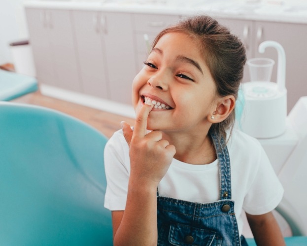 Young girl pointing to her smile during dental checkup and teeth cleaning visit
