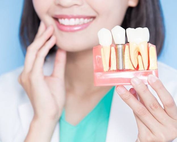 implant dentist in North Providence holding a dental implant model 