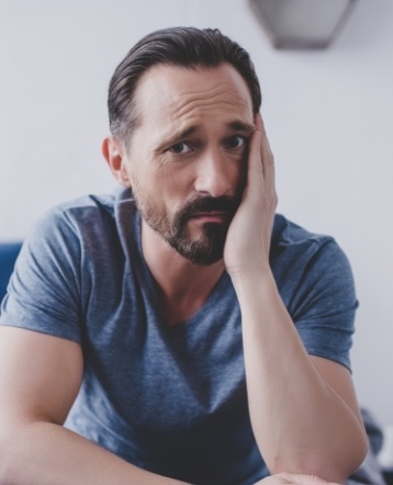 Man in need of emergency dentistry holding cheek in pain