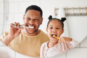 Dad and daughter brushing their teeth together in the bathroom mirror